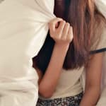 Young woman holding comforter over her face